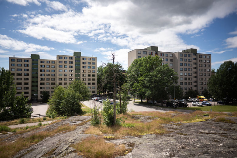 Kerrostalojen edustalla näkyy parkkipaikka, puita ja kalliota.