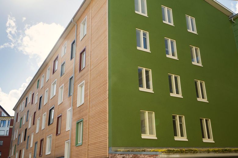 Värikässeinäisen kerrostalon katon yläpuolella näkyy sininen taivas.