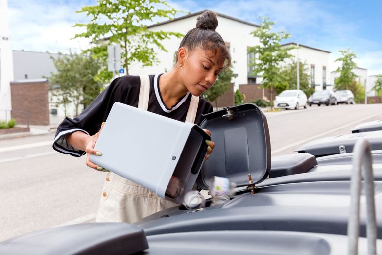 A woman empties glass waste into a waste container.