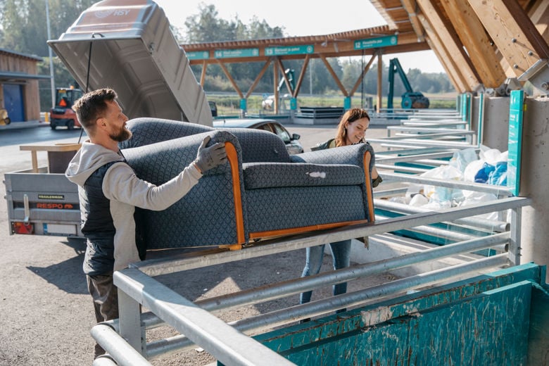 Mies ja nainen nostavat yhdessä sohvan Sortti-asemalla. Sohva on vanha ja menossa kierrätykseen.