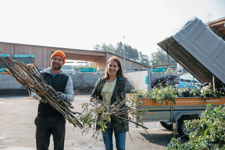 A woman and a man unloading brushwood from a trailer.