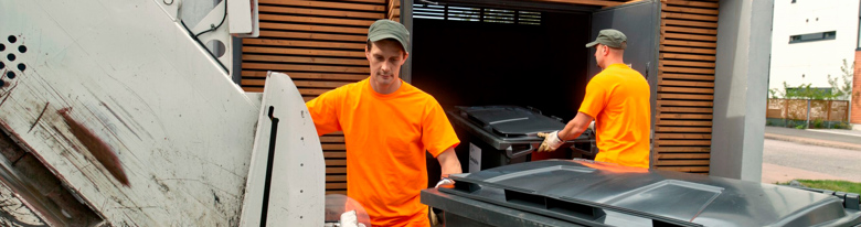Two men are emptying waste containers into a refuse truck. The housing company’s waste collection point can be seen in the background.