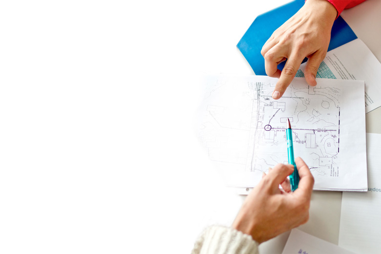 Kaksi henkilöä tutkii pöydällä olevaa paperia. Vain heidän kätensä näkyvät. Toisella on kynä ja toinen osoittaa jotakin.