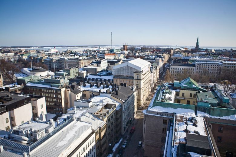 A wintry urban landscape shot from roof height. Blue sky, dense building formations and snow on top of the roofs.